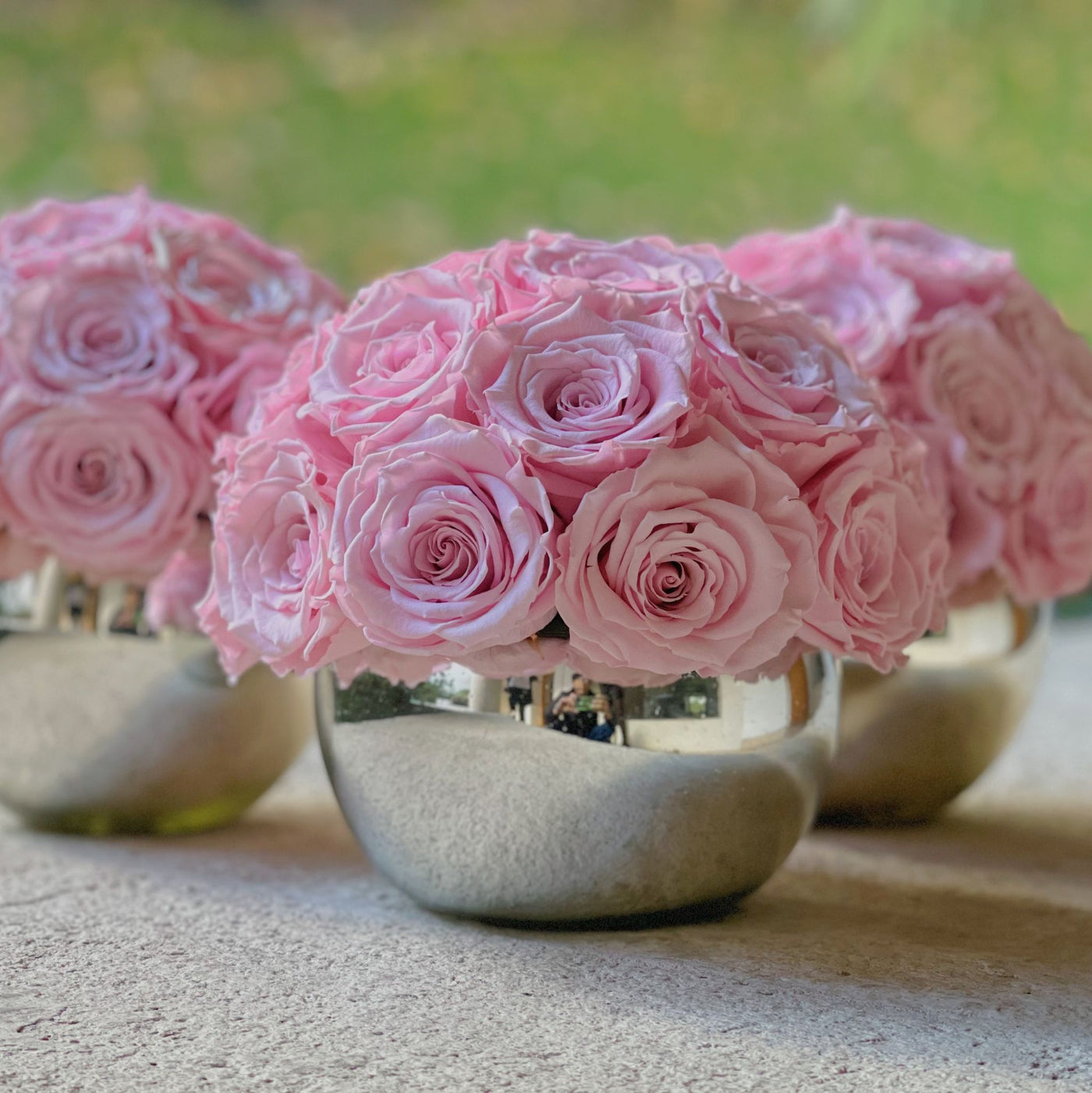 Hermosas rosas eternas de un color rosado suave casi dulce, colocadas sobre 3 jarrones de vidrio soplado con acabado de espejo.